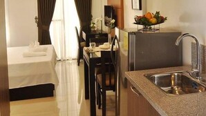 A compact hotel room with a bed, a small dining table, a kitchen area with a sink, and a refrigerator. - Rishan Village Residences (Angeles City)