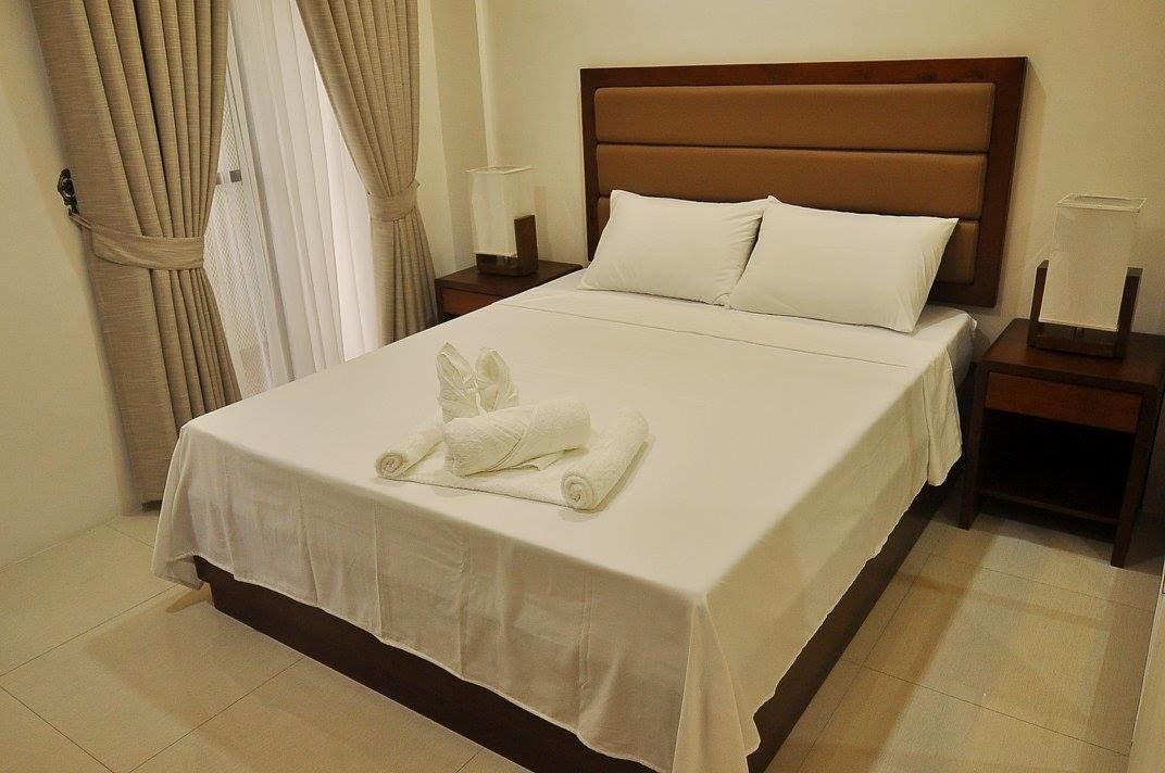 A neatly made bed with white linens, a wooden headboard, and a pair of towels on the bed.