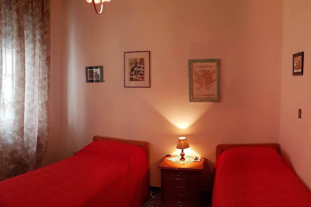 A bedroom with two single beds, a bedside table with a lamp, and three framed pictures on the wall.