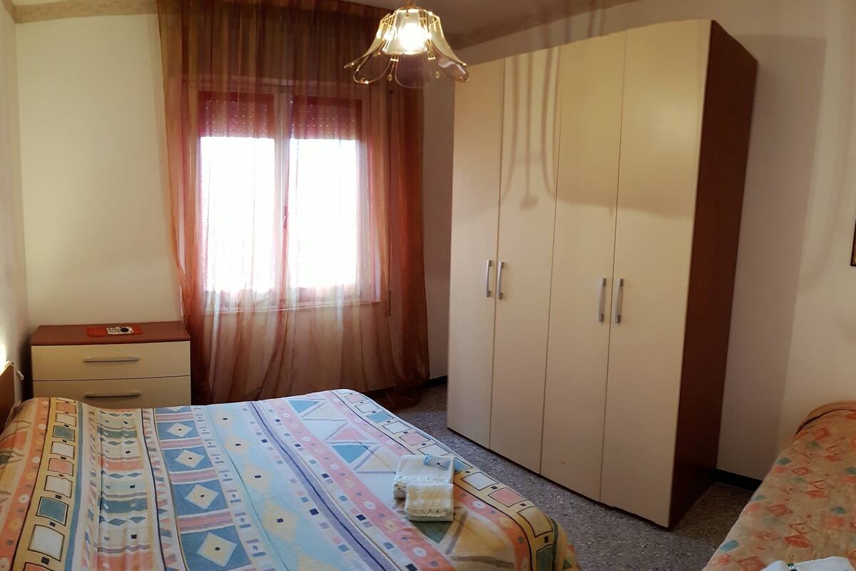 A bedroom with a bed, a wardrobe, a bedside table, and a window with curtains.