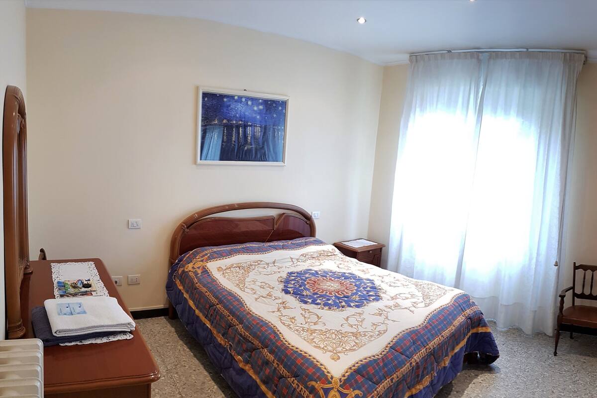 A bedroom with a bed, a nightstand, a chair, a wardrobe, and a window with curtains.
