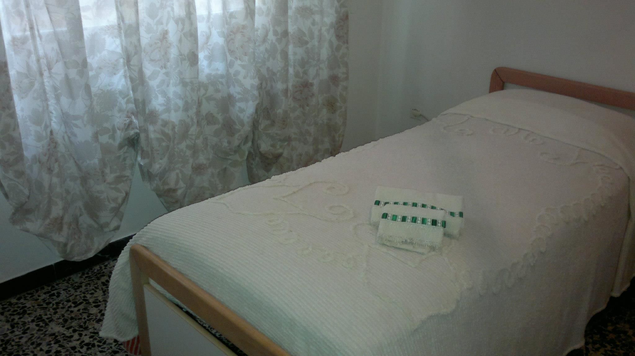 A single bed with a white bedspread and a green and white pillow.