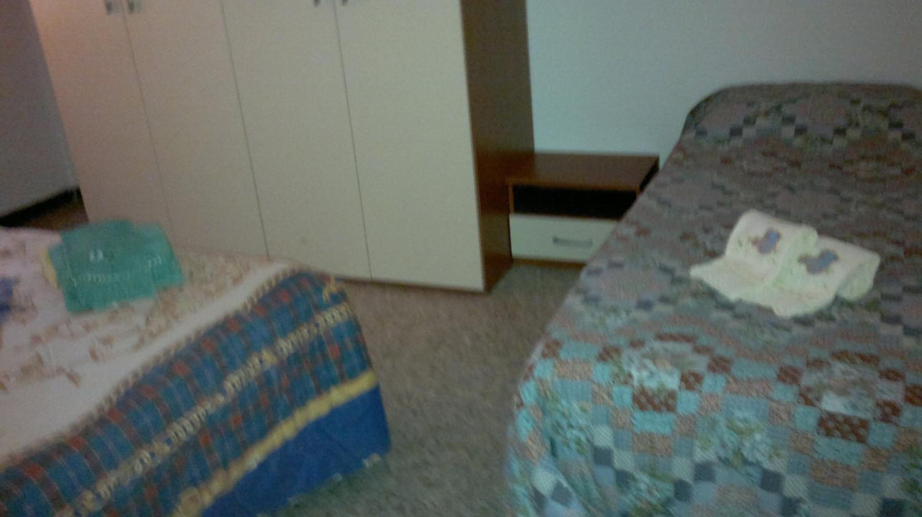 A bedroom with two beds, a wardrobe, and a small table.