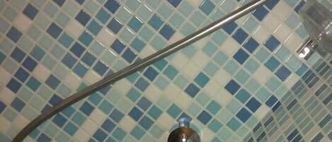 Un espacio de ducha con azulejos, un cabezal de ducha de metal y un cerramiento de vidrio.