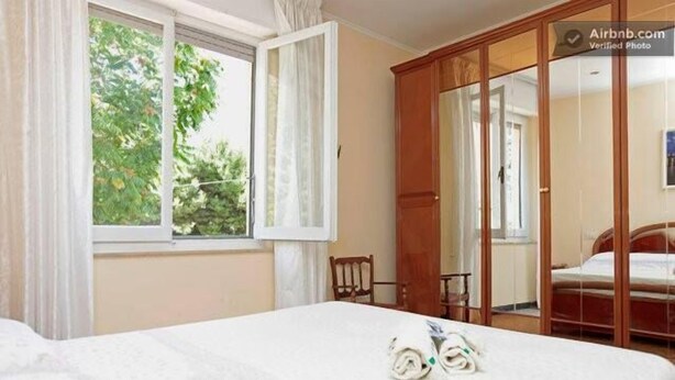 A hotel room with a bed, a window with curtains, a wooden wardrobe, and a mirror. - B&B In Centro (San Benedetto del Tronto)