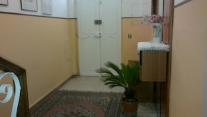 A hallway with a white door, a small potted plant, a decorative vase with flowers, and a patterned rug on the floor. - B&B In Centro (San Benedetto del Tronto)