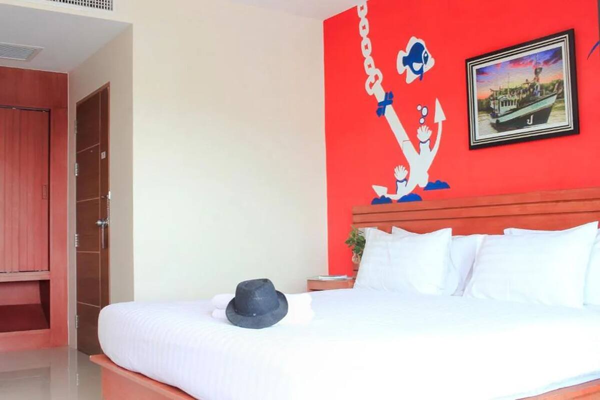 A hotel room with a large bed, a red accent wall, and a framed picture of a boat.
