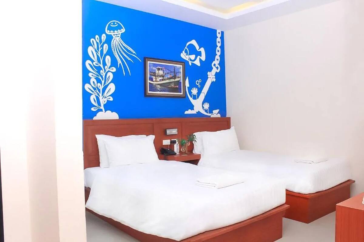 A hotel room with two beds, a blue wall with white marine-themed artwork, and a framed picture of a boat.