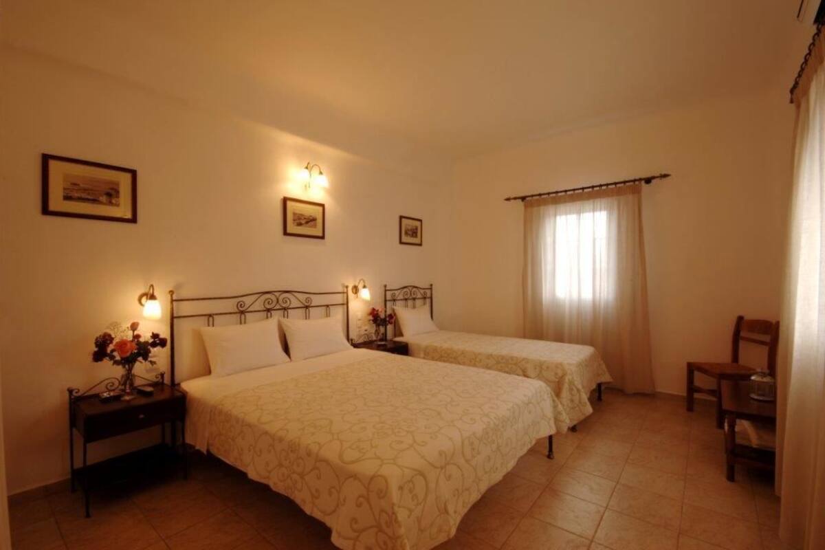 A hotel room with two beds, a nightstand with a lamp, a chair, and a window with curtains.
