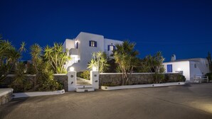 A white building with a stone wall and palm trees in front. - Stavroula Studios (Mykonos)