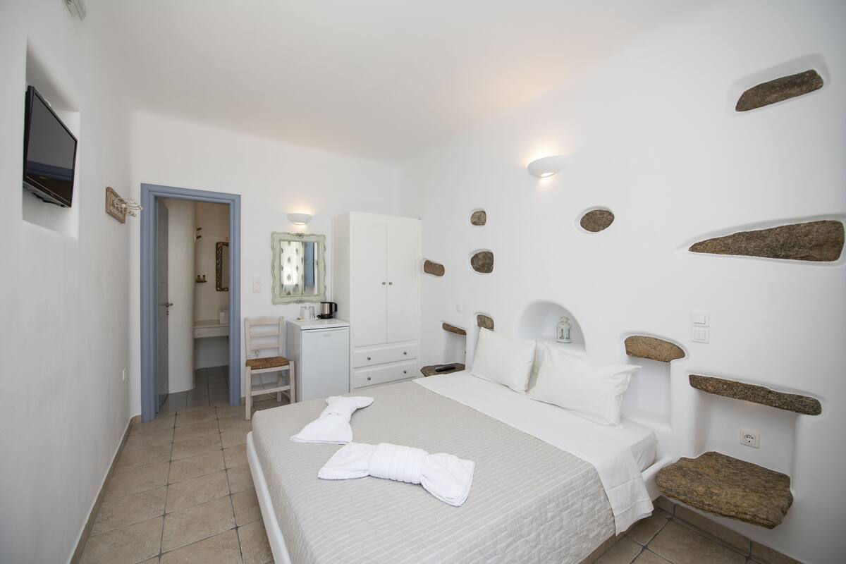 A bedroom with a bed, a dresser, a mirror, and a television.