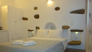 A bedroom with a bed, a wardrobe, and a wall with embedded rocks. - Stavroula Studios (Mykonos)