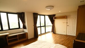 Ein Schlafzimmer mit großem Fenster, einem Bett, einem Schreibtisch und einem Kleiderschrank.