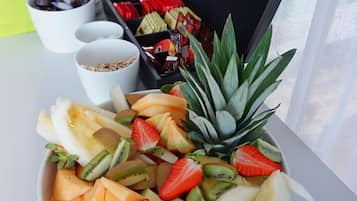 A fruit bowl on a table with a tray of snacks and a box labeled "TWININGS" in the background.