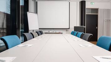 A conference room with a long table, chairs, a projector screen, and a whiteboard.