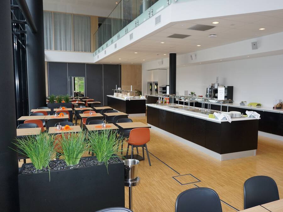 Un comedor moderno con varias mesas y sillas, una barra central con un lavamanos y vista al piso superior.