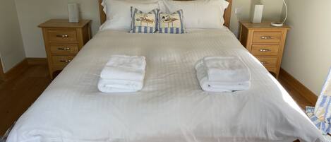 A neatly made bed with two folded towels, wooden headboard, bedside tables with lamps, and a framed picture on the wall.