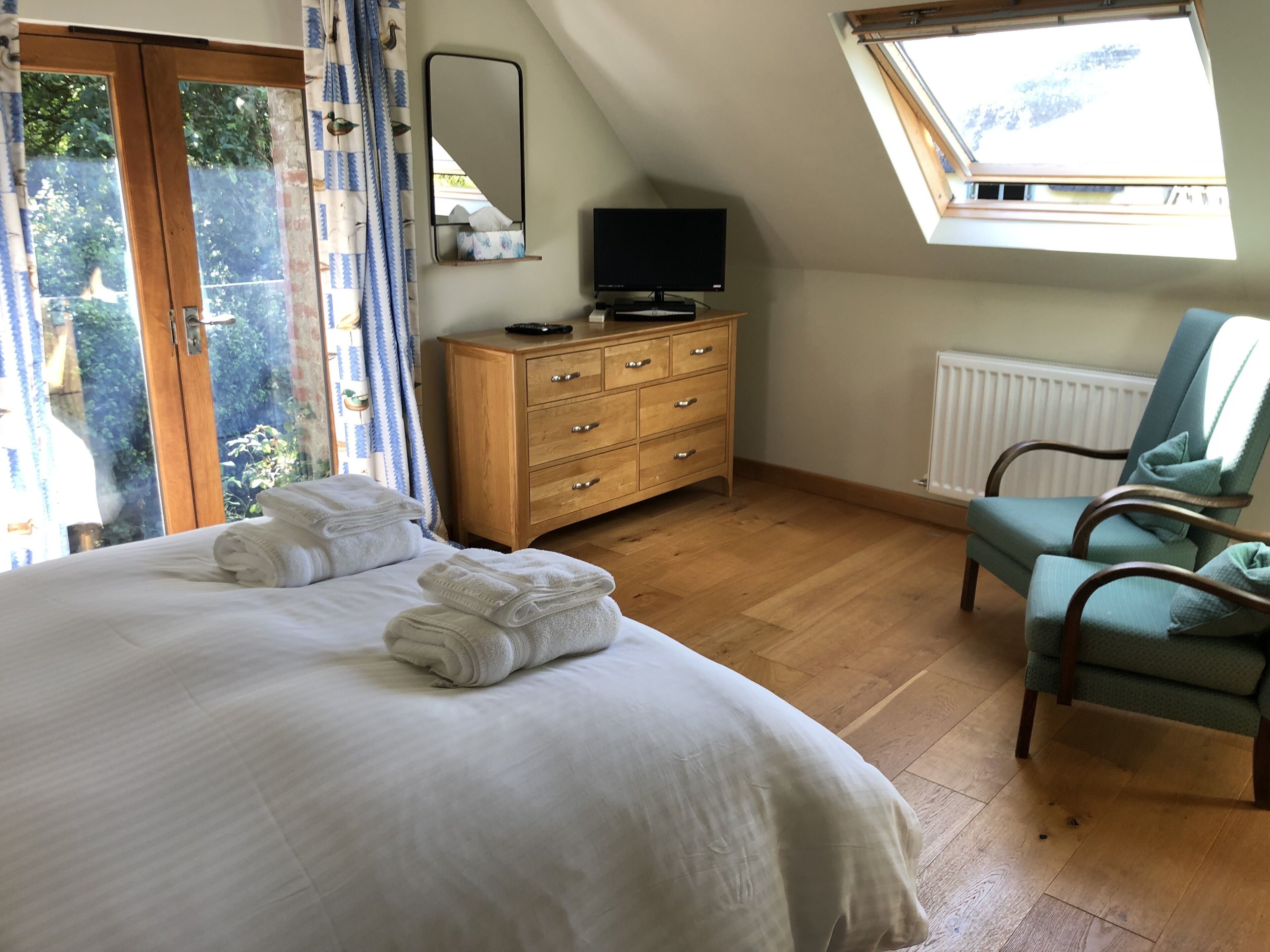 A bedroom with a bed, a wooden dresser, a television, a chair, and a skylight.