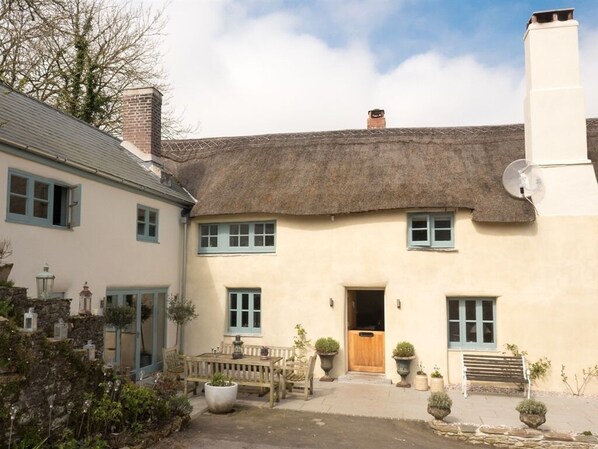 A traditional building with a thatched roof, a wooden door, and a small garden with potted plants and a bench.