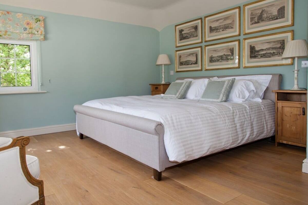 A bedroom with a bed, wooden floor, a window, and framed pictures on the wall.