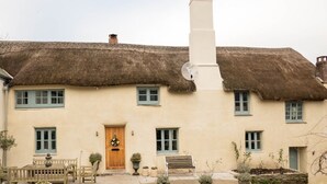 Ein traditionelles Haus mit einem Strohdach, einer Mittelinsel und Fenstern, mit einer Bank im Vorgarten.