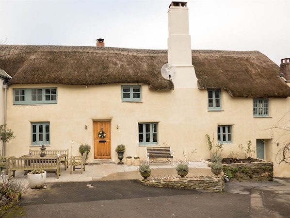 A traditional thatched-roof house with a central door, windows, and a bench in the front yard. - Glebe Farm B&B (Kingsbridge)