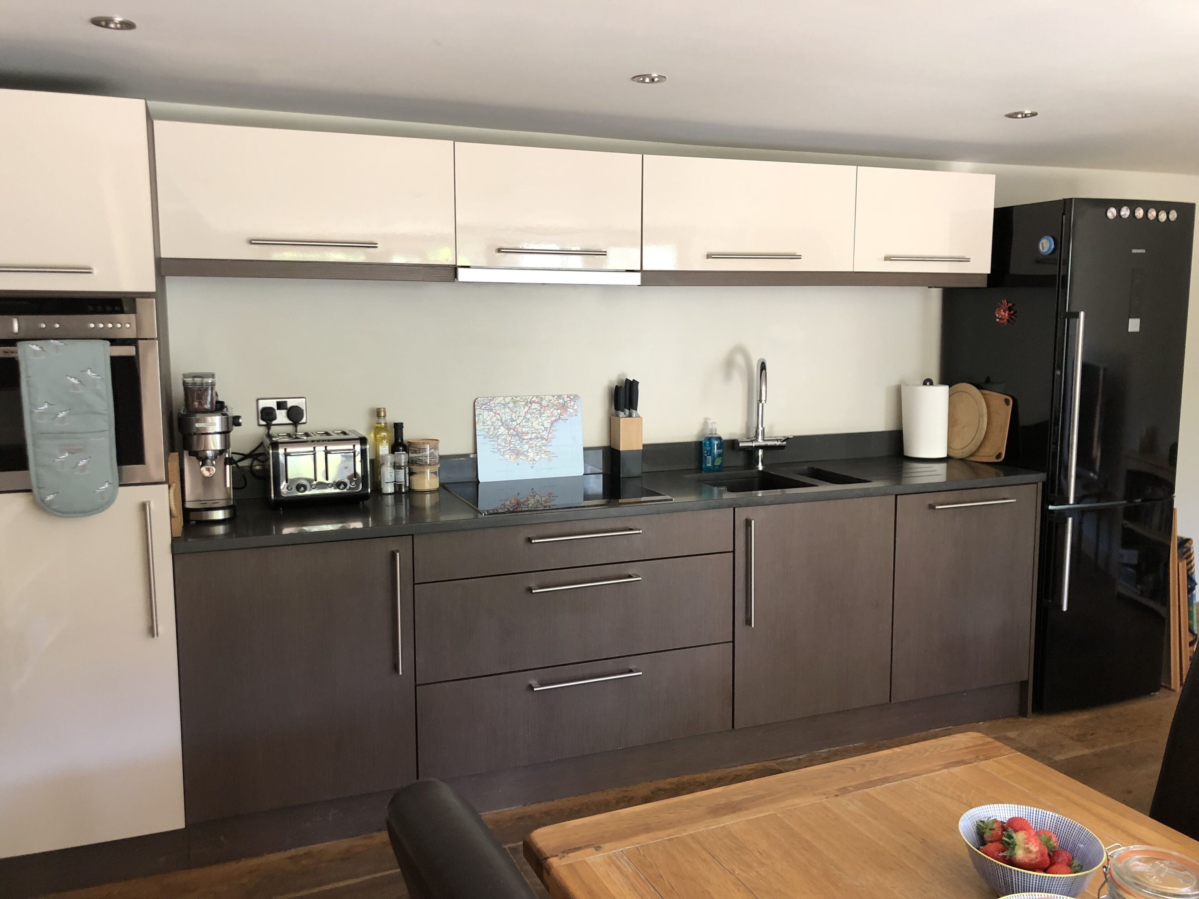 Een moderne keuken met donkere kastjes, roestvrijstalen apparatuur, een houten eettafel en een schaal met aardbeien.
