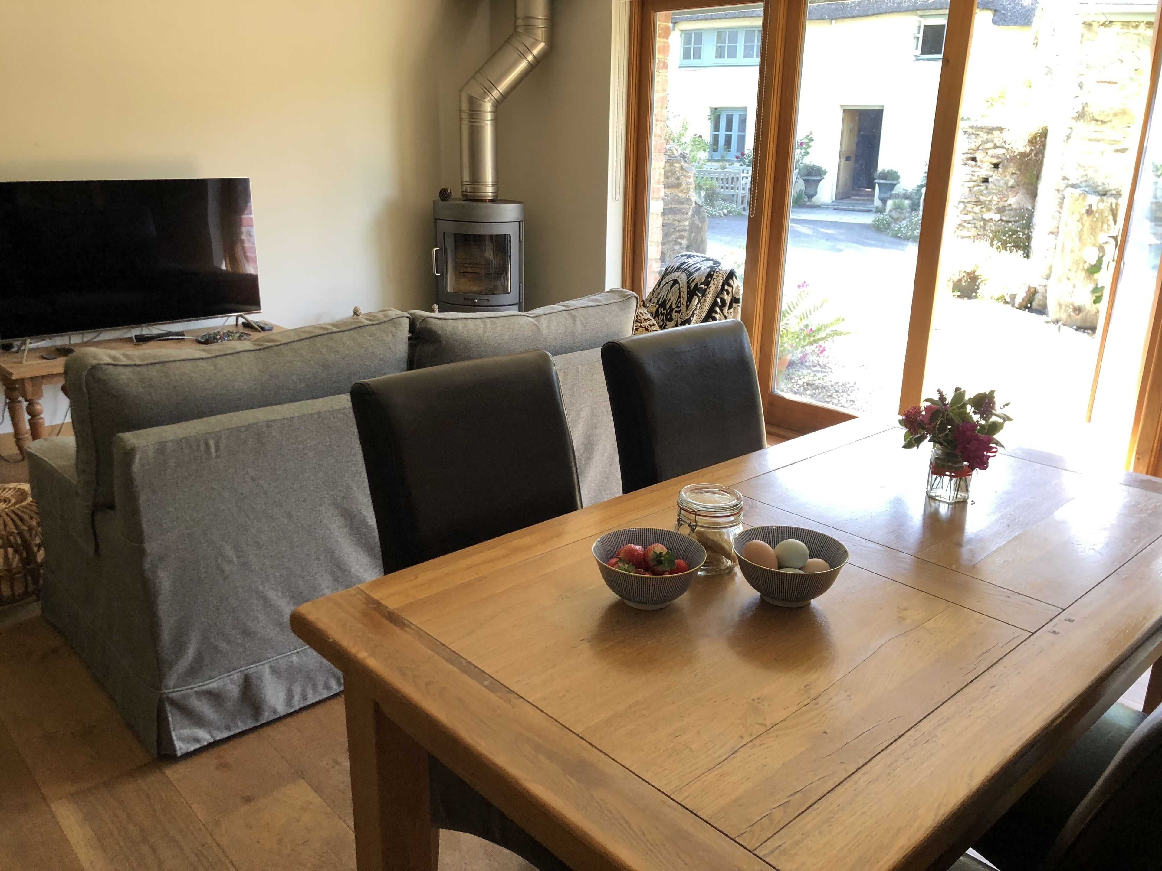 A cozy living room with a sofa, a wooden table with bowls and eggs, a TV, and a wood-burning stove.