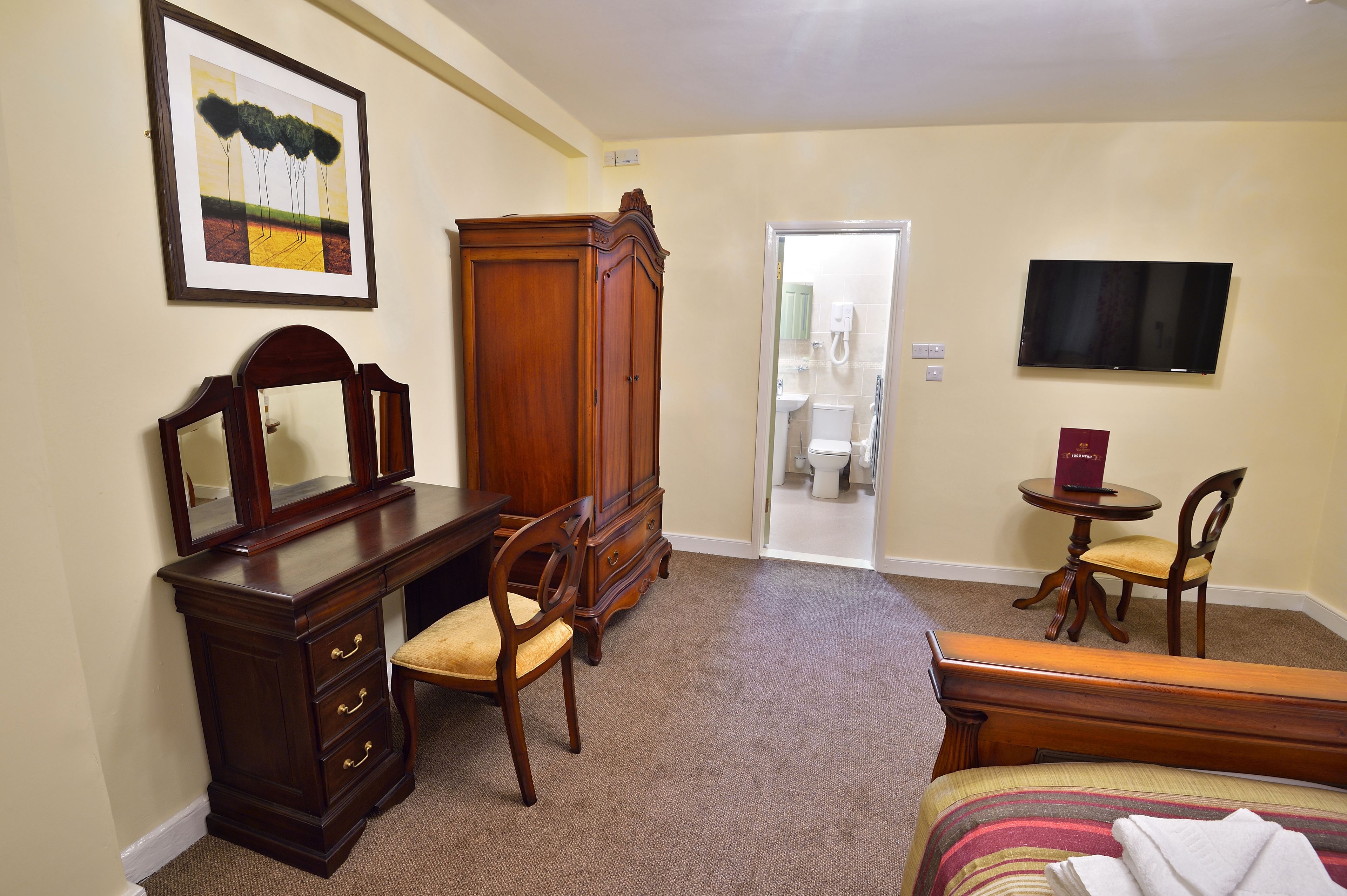A hotel room with a wooden dresser, a chair, a bench, a television, and a framed picture on the wall.
