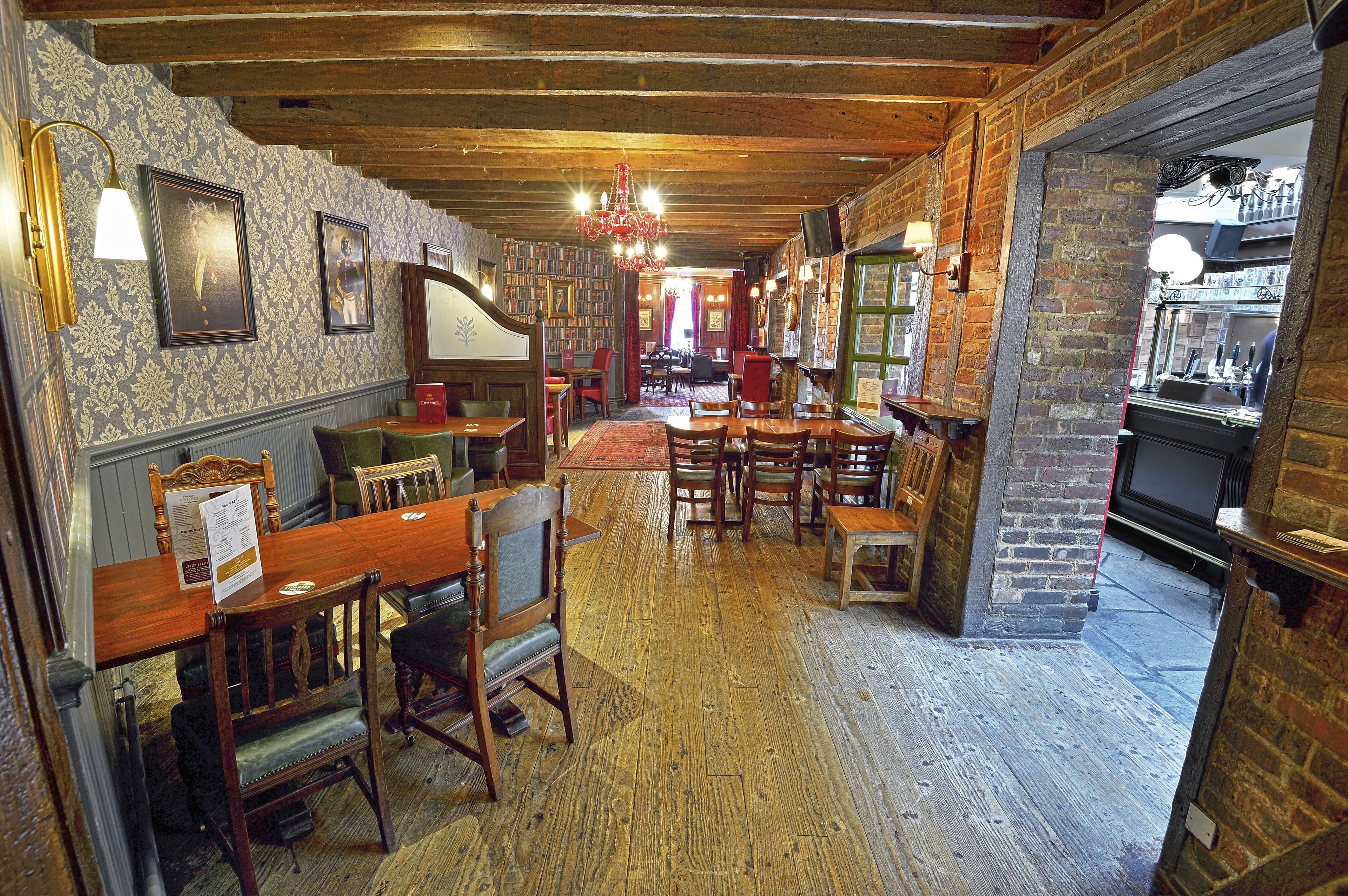 A traditional inn with wooden floors, brick walls, and classic furnishings. There are multiple wooden tables and chairs arranged for dining.