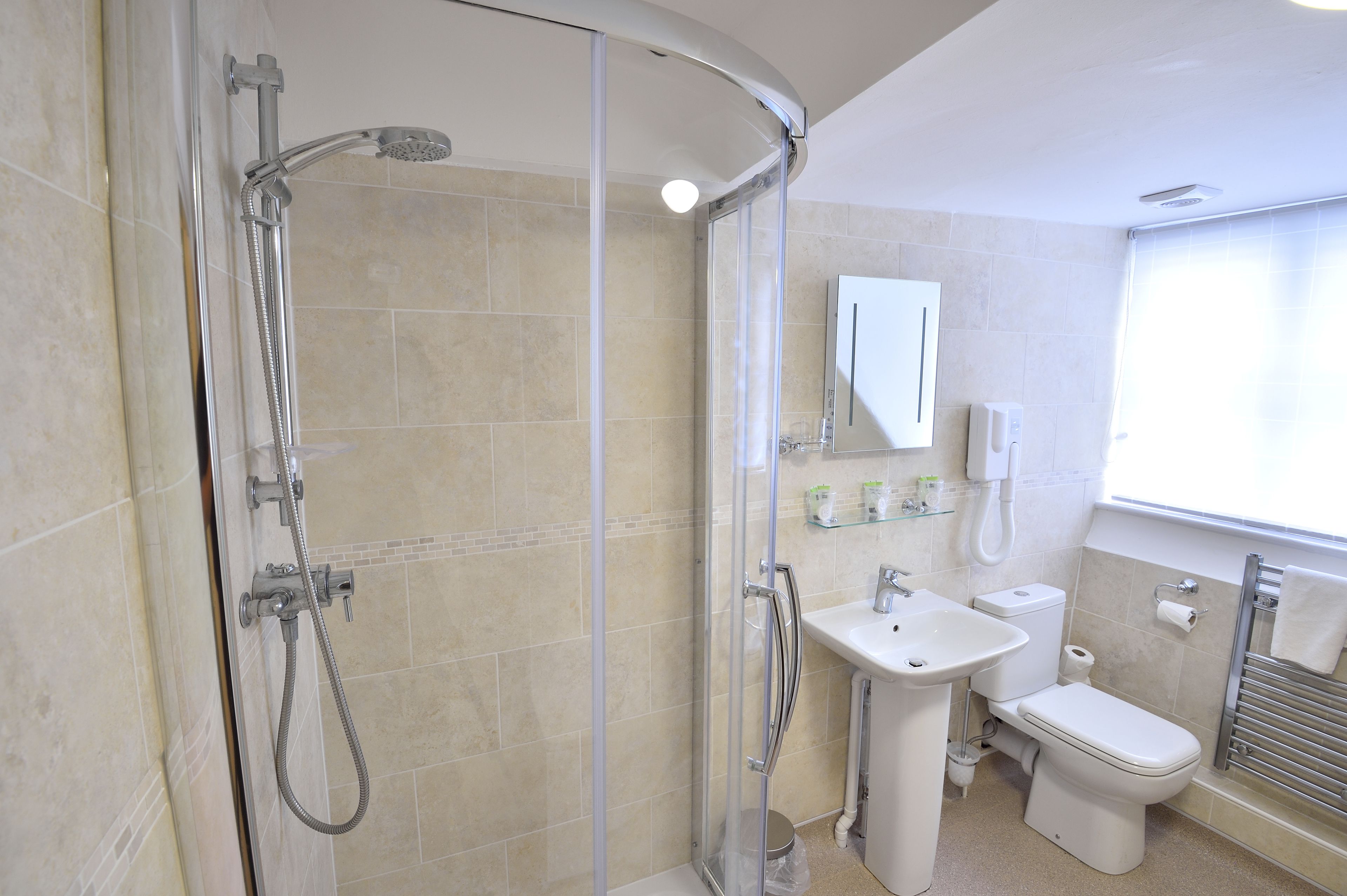 Un baño moderno con ducha envuelta en vidrio, lavamanos, inodoro y espejo.