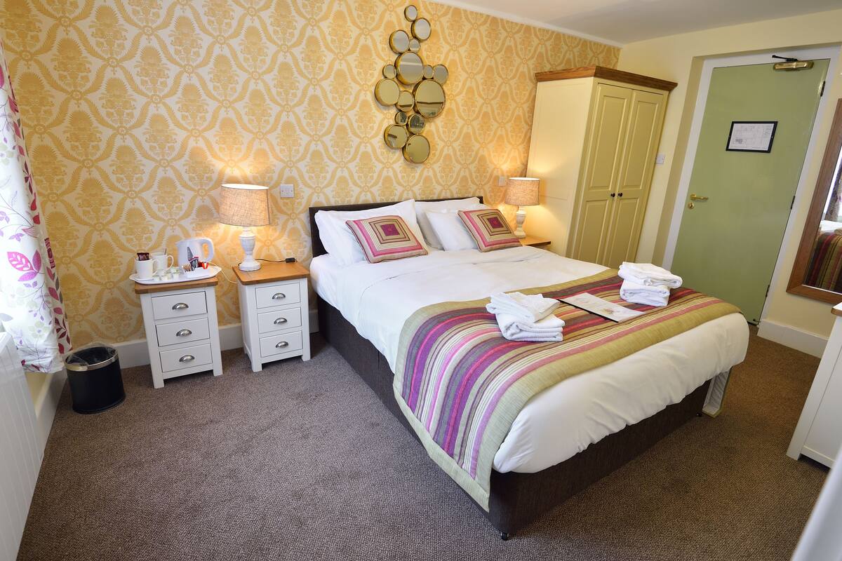 A neatly made bed with a striped blanket, two bedside tables with lamps, a mirror on the wall, and a green door.