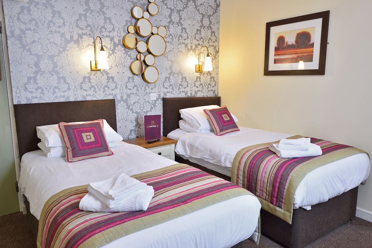 A hotel room with two beds, a decorative wall with a mirror and wall sconces, and a framed picture on the wall.
