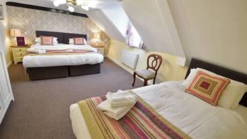 Un dormitorio con dos camas, una silla, una mesita de noche, una lámpara y un papel tapiz estampado.