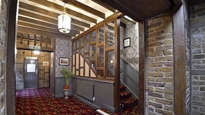 A hallway with patterned carpet, wooden beams, and a fire exit sign. - The Royal Victoria & Bull Hotel (Dartford)