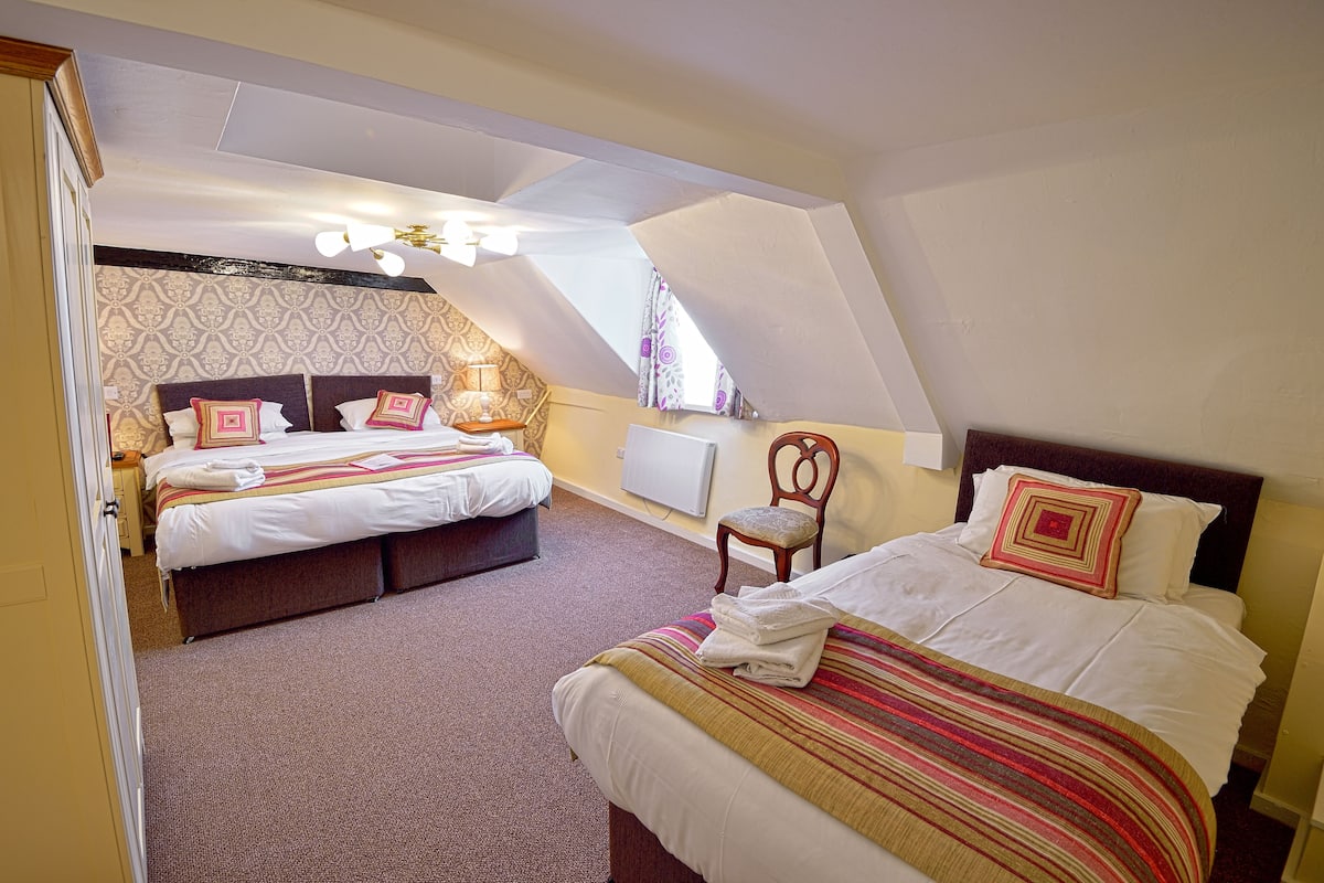 A hotel room with two beds, a sitting area, and a window with curtains.