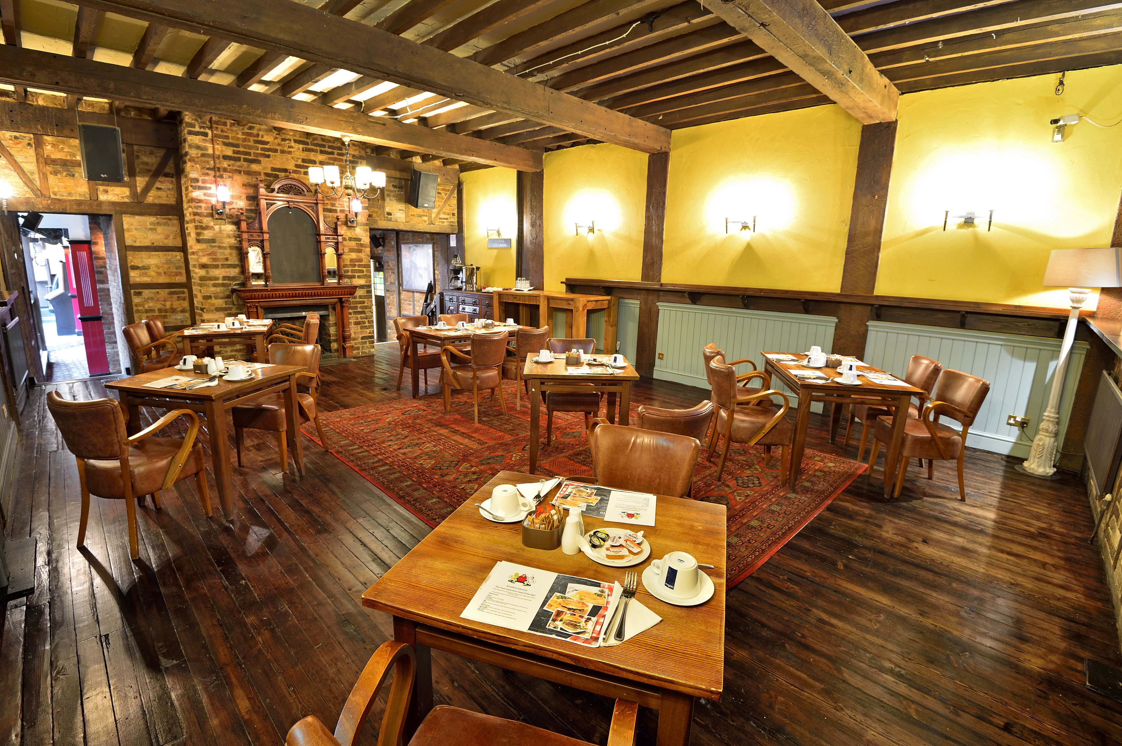 A restaurant with wooden tables and chairs, a brick wall, and a yellow wall with lights.