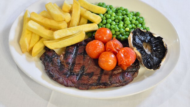 Ein Teller mit einem Steak, Pommes, Erbsen, Kirschtomaten und einem Pilz.