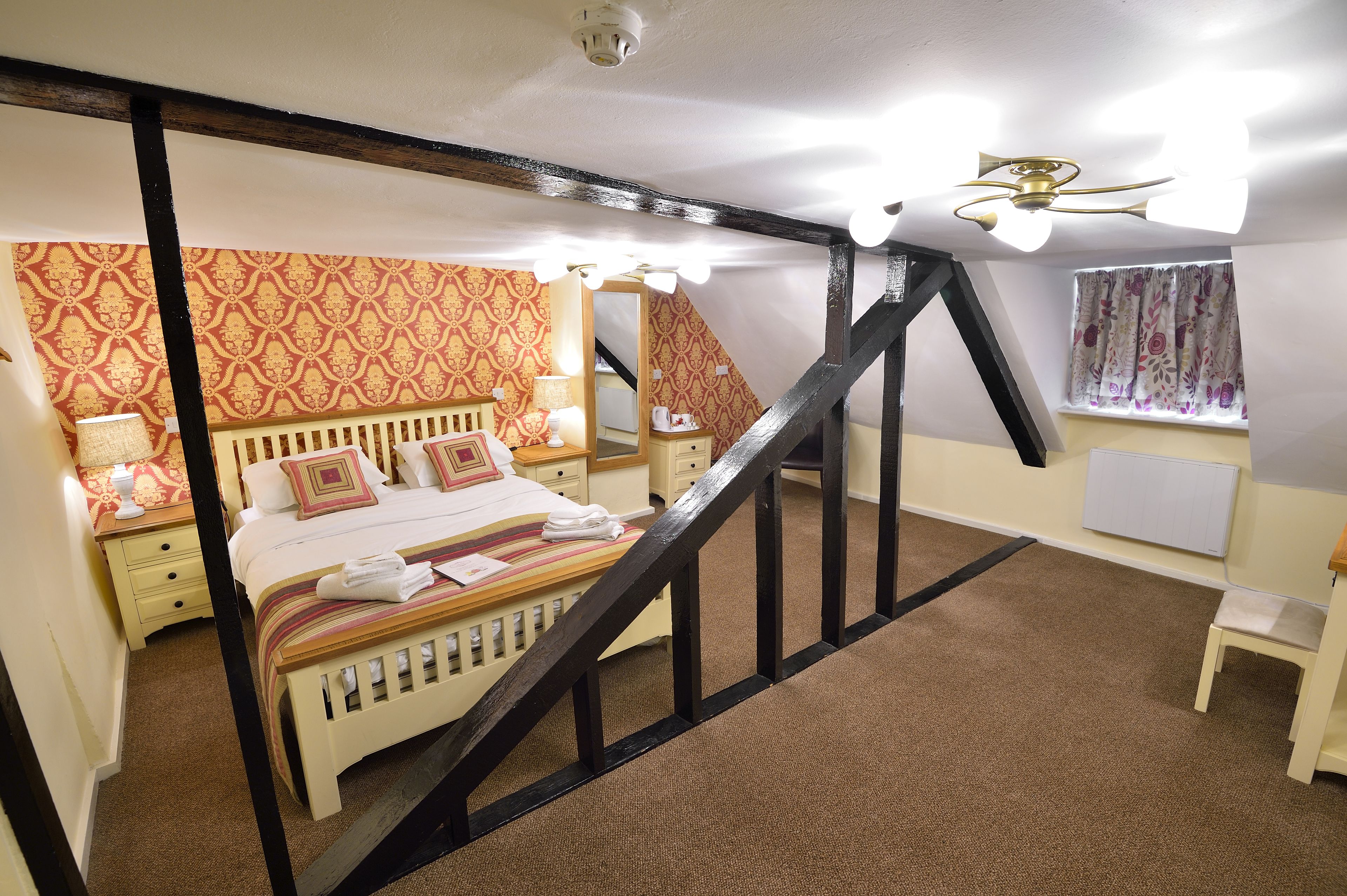 Un dormitorio con cama, mesitas de noche, una escalera de madera y una ventana con cortinas.