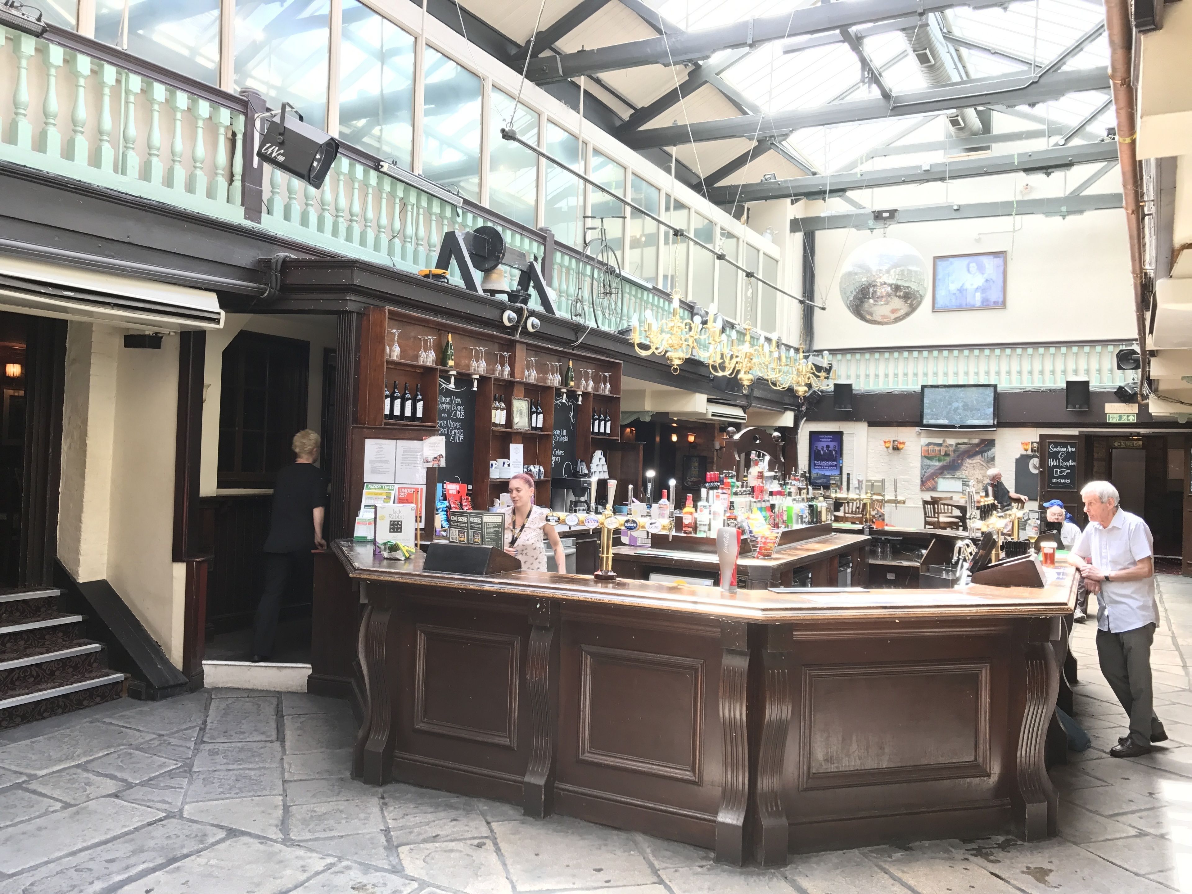 A bar area with a counter, shelves with bottles, and a chandelier.