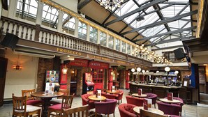 A spacious indoor area with multiple seating arrangements, including round tables and chairs, and a bar area with a counter and stools. - The Royal Victoria & Bull Hotel (Dartford)