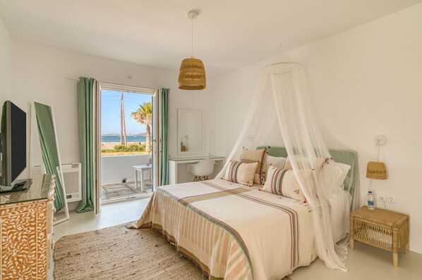 A bedroom with a bed, a TV, a desk, and a view of the sea. - Villa Bellonia (Paros)