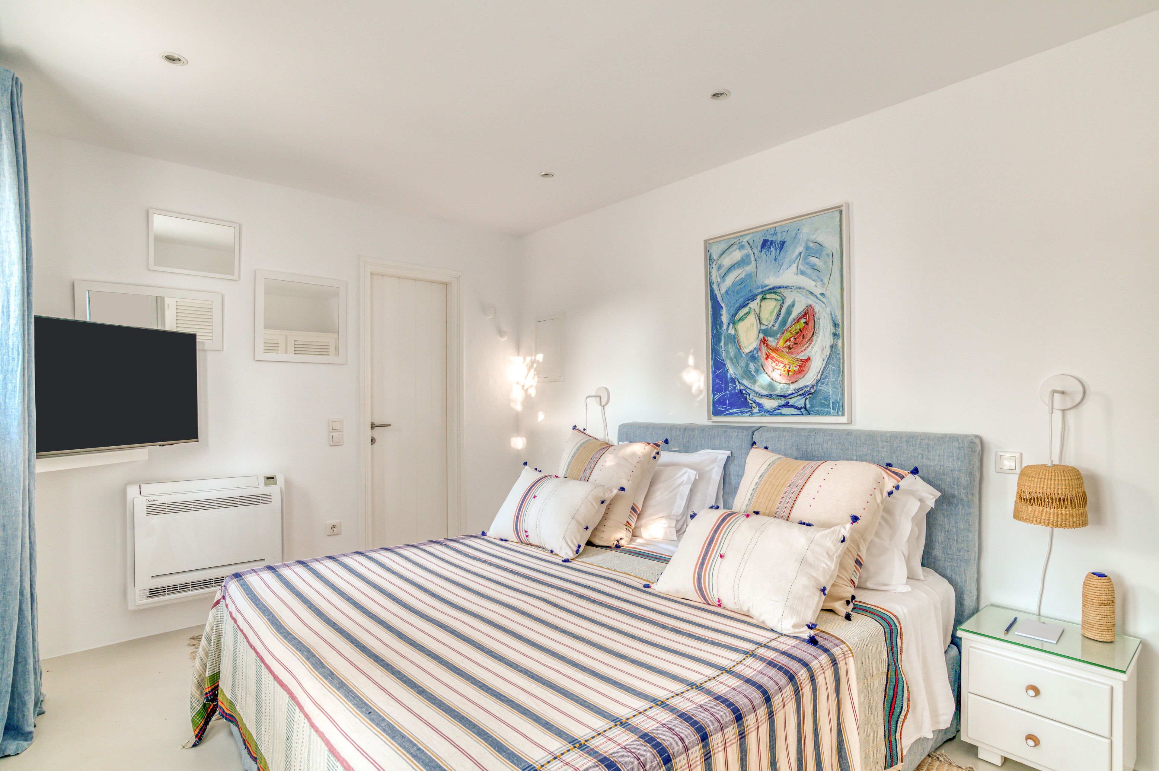 A bedroom with a bed, bedside tables, a flat-screen TV, a painting, and a lamp.