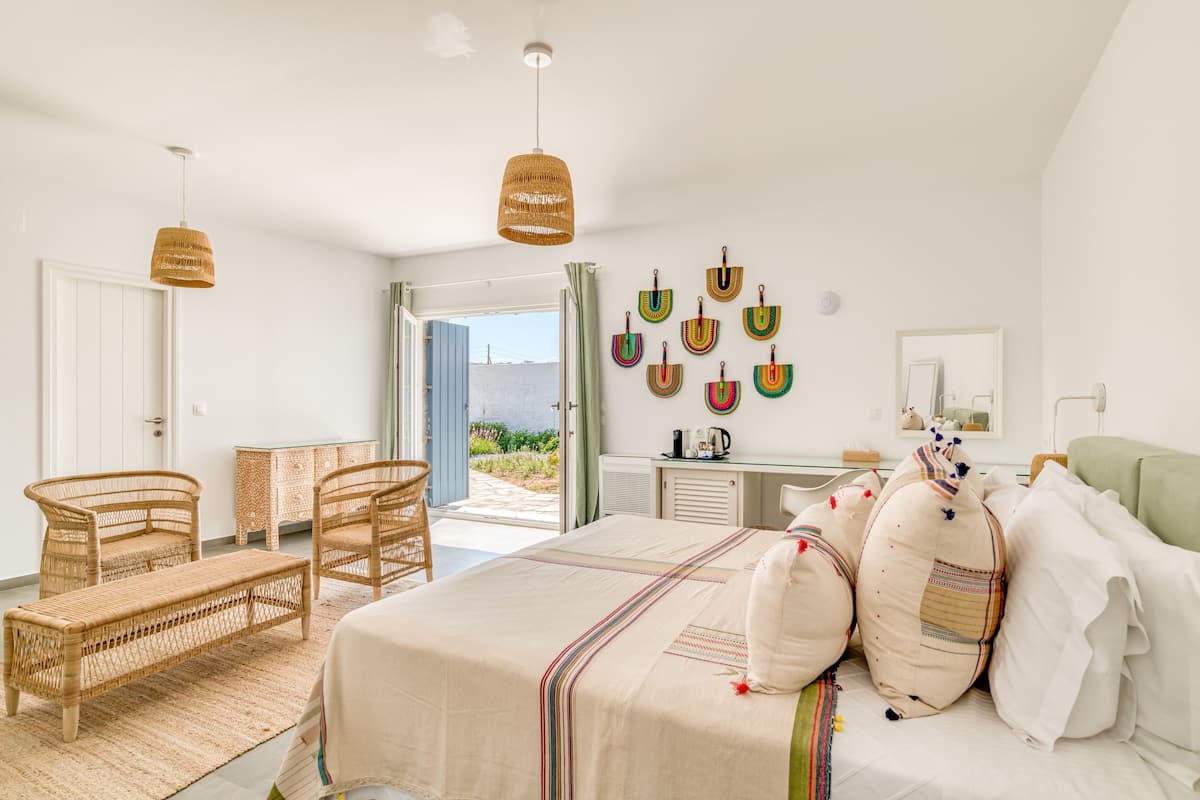 Un dormitorio con una cama, dos sillones de mimbre, una mesita, un escritorio y vistas al exterior.