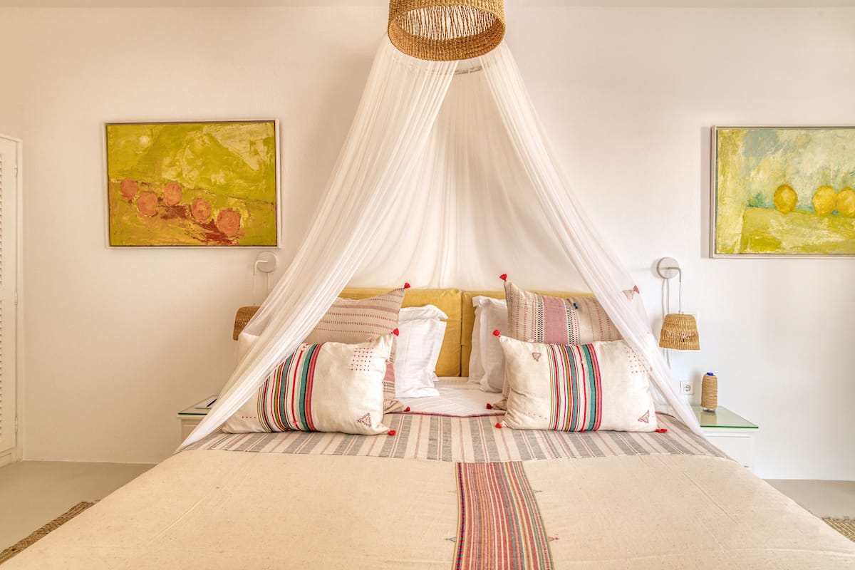 Una cama con dosel, almohadas a rayas y dos cuadros en la pared.
