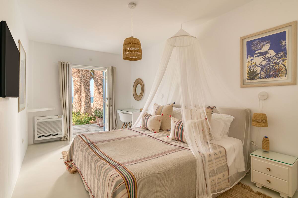 Un dormitorio con cama con dosel, mesita de noche y vistas al exterior.