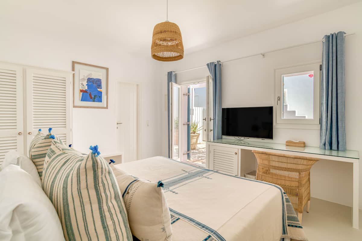 Un dormitorio con cama, escritorio, televisor y silla de mimbre.