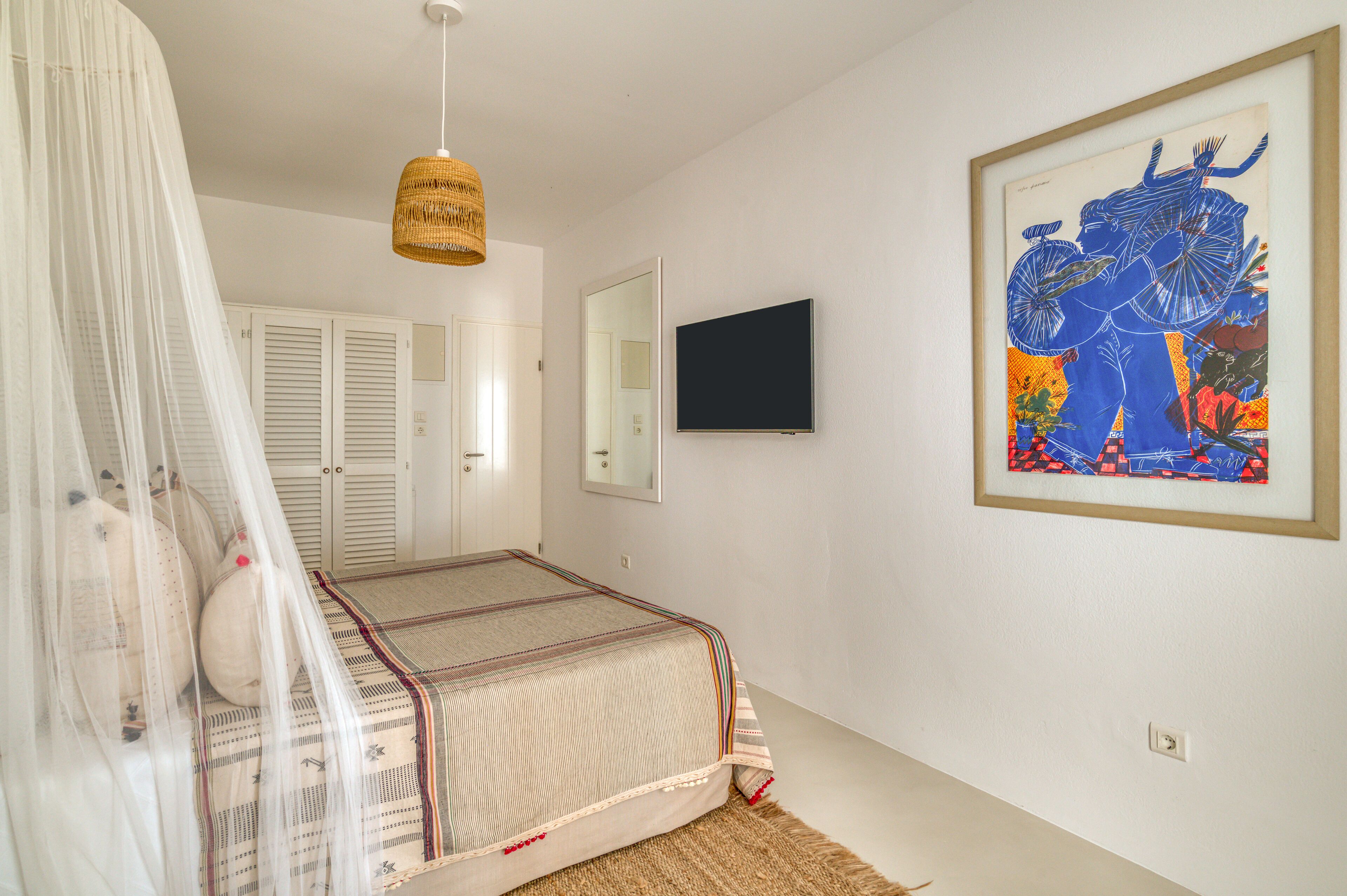 A bedroom with a bed, a television, a framed artwork, and a hanging light fixture.