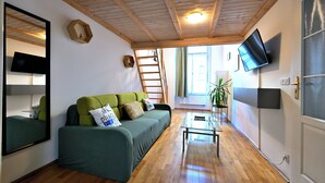 A cozy living room with a green sofa, wooden flooring, a small table, and a TV mounted on the wall. - Hybernska Apartments (Prague)