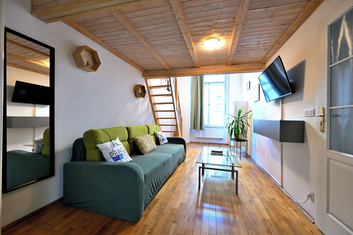 A cozy living room with a green sofa, wooden flooring, a small table, and a TV mounted on the wall.
